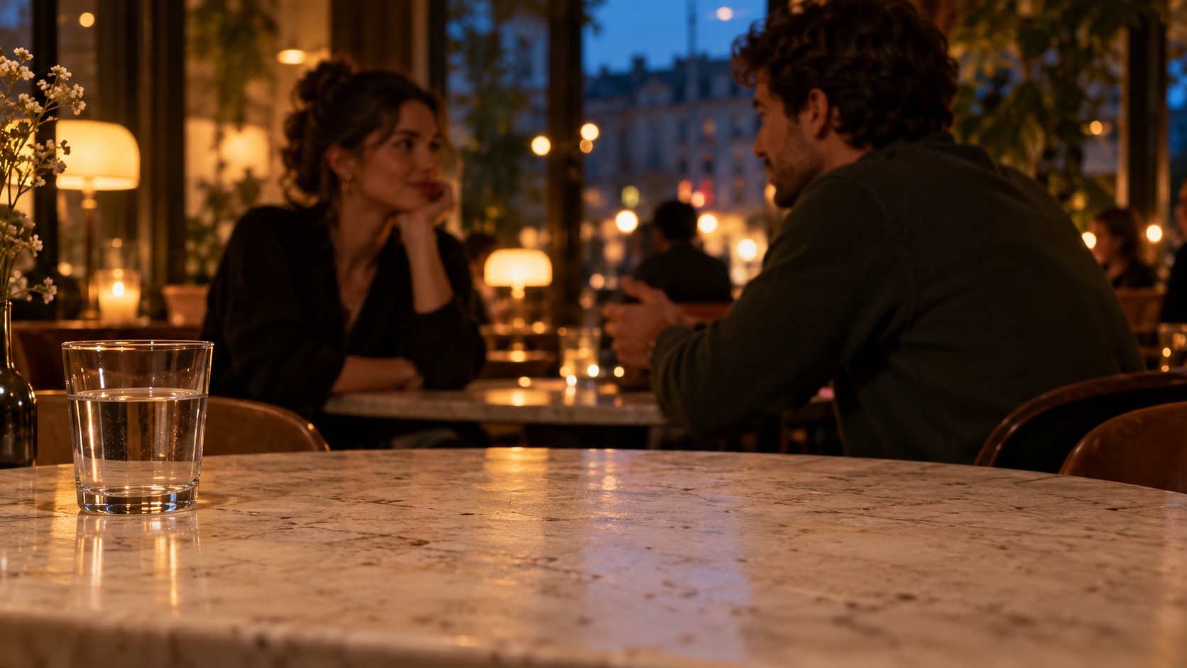 Two people talk in a café, with a marble table in the foreground.